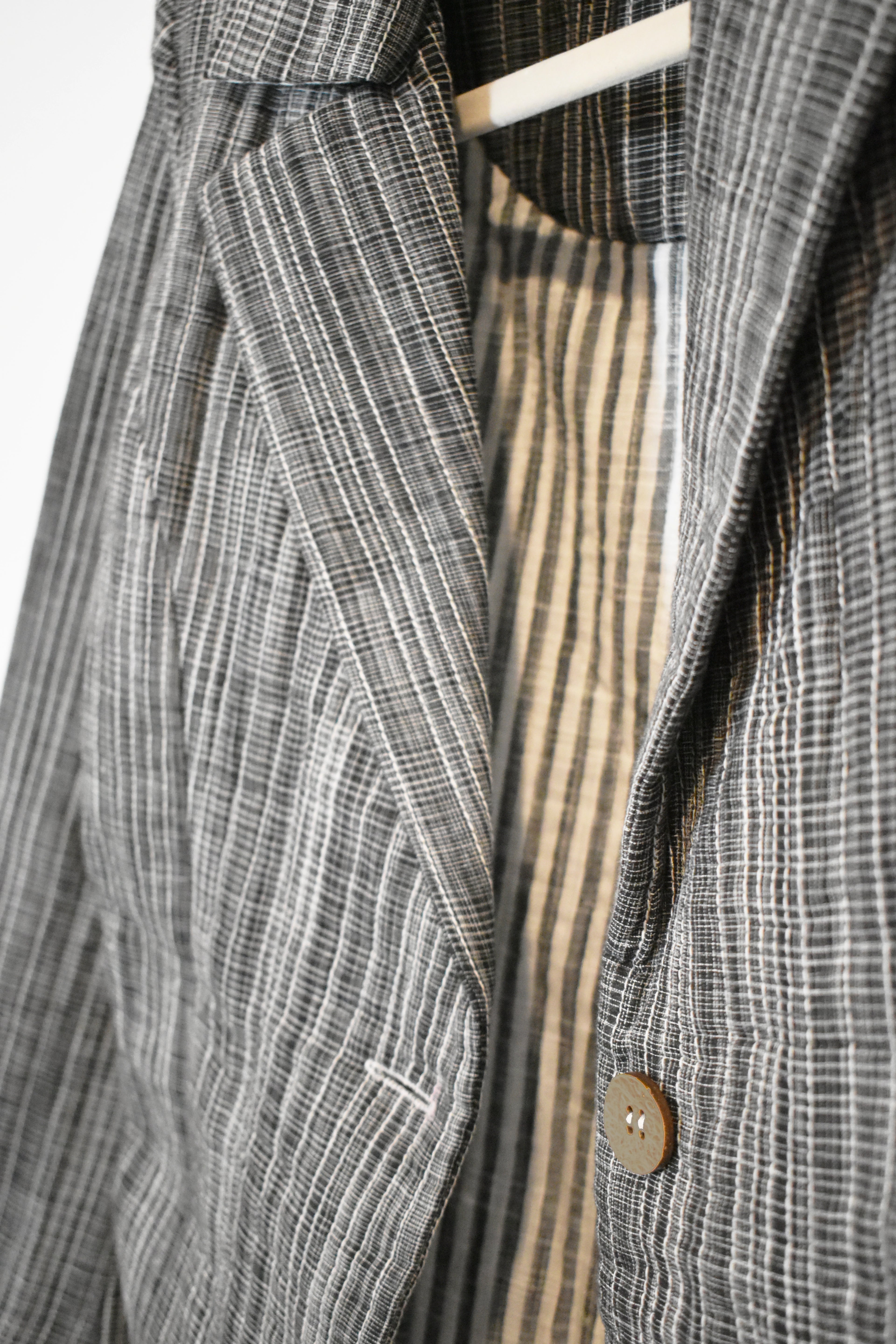 Close-up of a gray plaid coat with a button on a white background